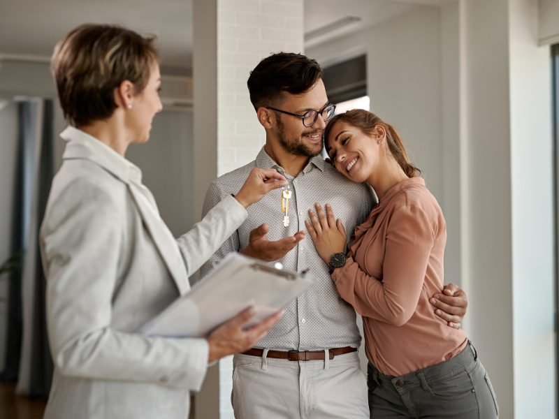 Young happy couple receiving keys of their new home from real estate agent.