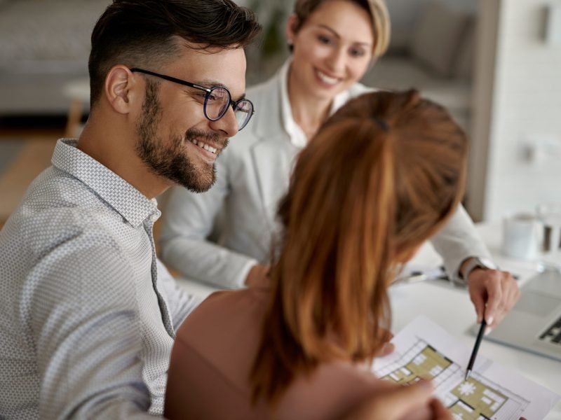 Young happy couple and their real estate agent having a meeting in the office. Focus is on man.